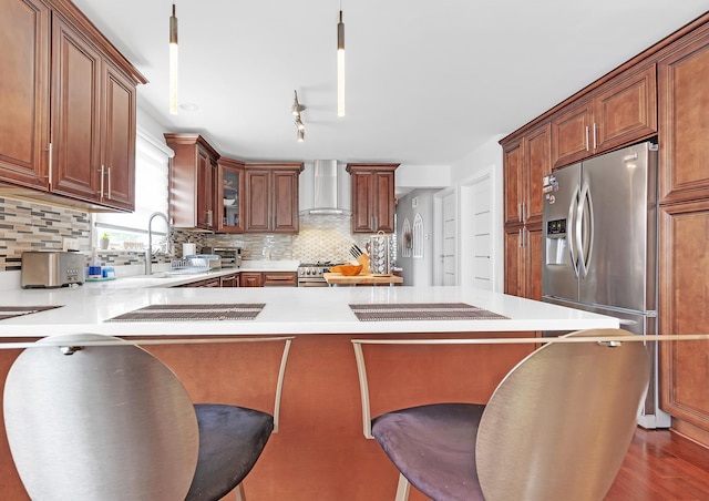 kitchen featuring a kitchen bar, sink, hanging light fixtures, appliances with stainless steel finishes, and wall chimney range hood