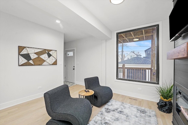 sitting room with light wood finished floors, baseboards, and a glass covered fireplace