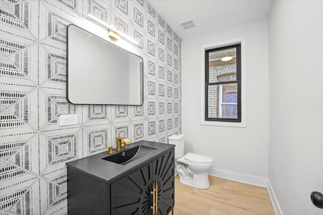 half bathroom with visible vents, toilet, vanity, wood finished floors, and baseboards