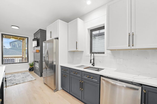 kitchen with light stone counters, light wood finished floors, stainless steel appliances, white cabinetry, and a sink