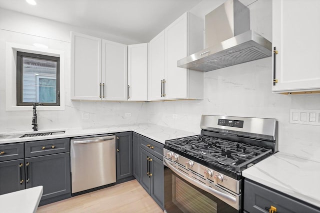 kitchen with wall chimney range hood, a sink, appliances with stainless steel finishes, and white cabinetry