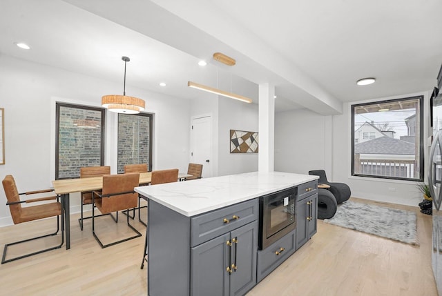 kitchen featuring black microwave, light wood finished floors, gray cabinets, and light stone counters