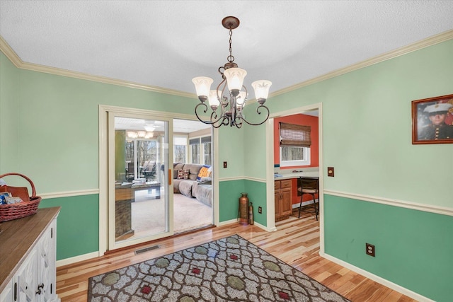 dining space with a notable chandelier, ornamental molding, light hardwood / wood-style floors, and a textured ceiling