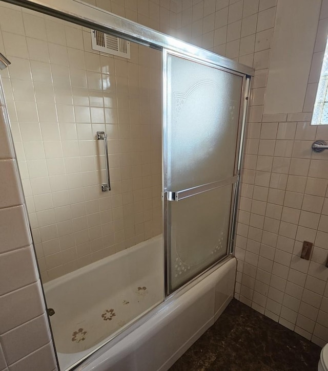 bathroom with combined bath / shower with glass door and tile walls