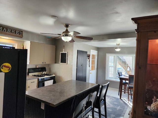 kitchen featuring range with gas cooktop, black fridge, light tile patterned floors, ceiling fan, and backsplash