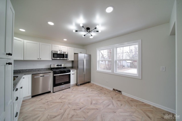 kitchen featuring white cabinetry, a notable chandelier, light parquet flooring, and appliances with stainless steel finishes