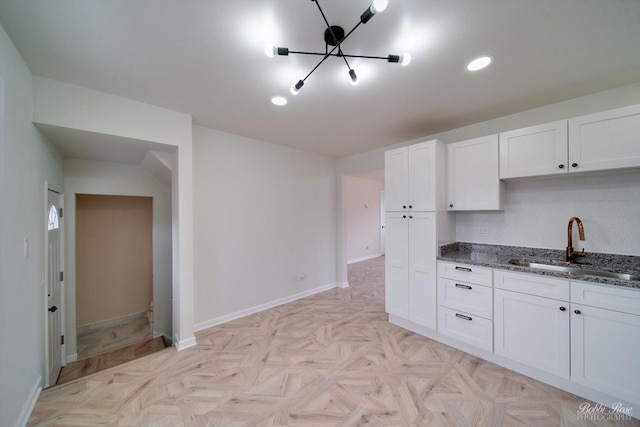 kitchen with sink, light parquet floors, dark stone counters, and white cabinets