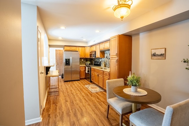 kitchen with stainless steel appliances, sink, decorative backsplash, and light wood-type flooring