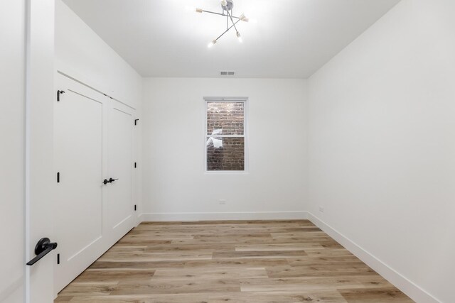 empty room with a notable chandelier and light wood-type flooring