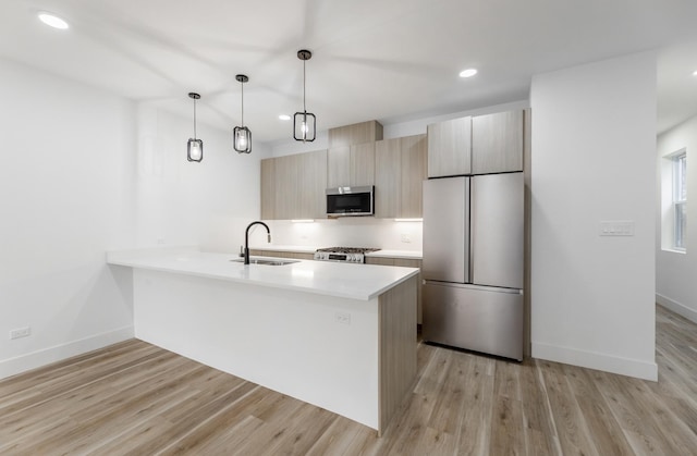 kitchen featuring sink, hanging light fixtures, stainless steel appliances, light brown cabinets, and light hardwood / wood-style flooring