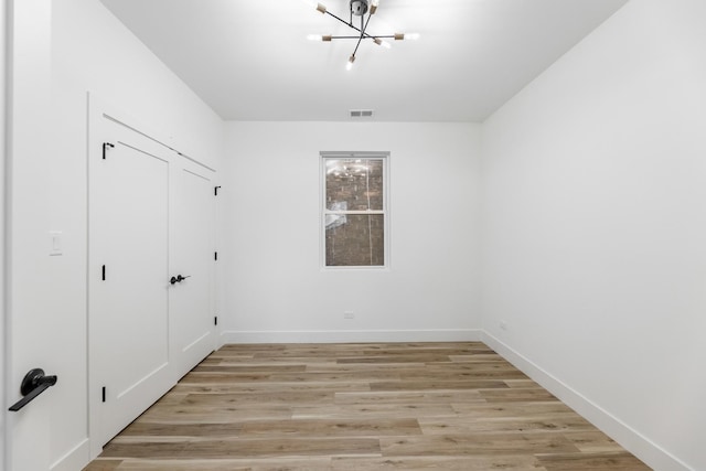 empty room with a chandelier and light hardwood / wood-style floors