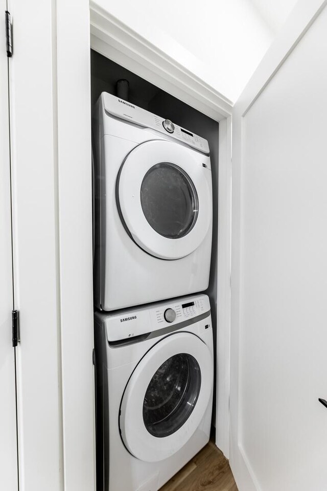 laundry room with hardwood / wood-style flooring and stacked washer and dryer