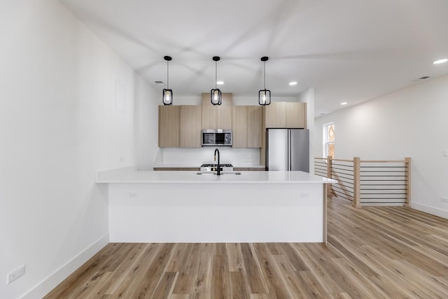 kitchen with light brown cabinetry, hanging light fixtures, sink, and appliances with stainless steel finishes