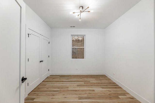 spare room with an inviting chandelier and light wood-type flooring