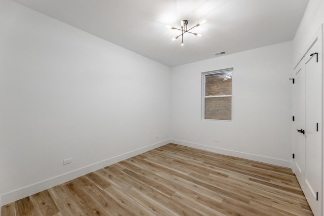 spare room with an inviting chandelier and light hardwood / wood-style floors