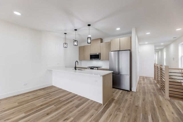 kitchen featuring appliances with stainless steel finishes, sink, light hardwood / wood-style flooring, and decorative light fixtures