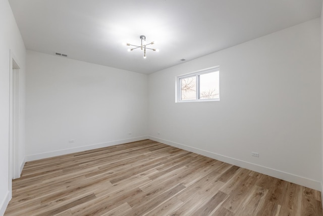 spare room with a notable chandelier and light wood-type flooring