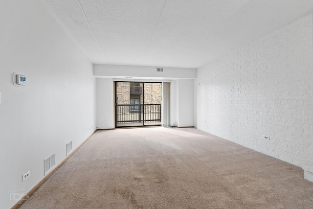 spare room featuring brick wall, light carpet, and a textured ceiling