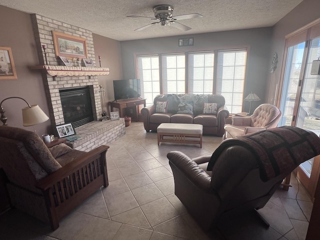 living room with ceiling fan, a fireplace, a textured ceiling, and light tile patterned floors