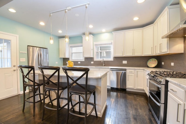 kitchen with a kitchen island, appliances with stainless steel finishes, sink, hanging light fixtures, and wall chimney exhaust hood