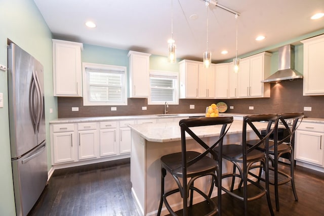 kitchen with sink, a breakfast bar area, stainless steel refrigerator, decorative light fixtures, and wall chimney exhaust hood