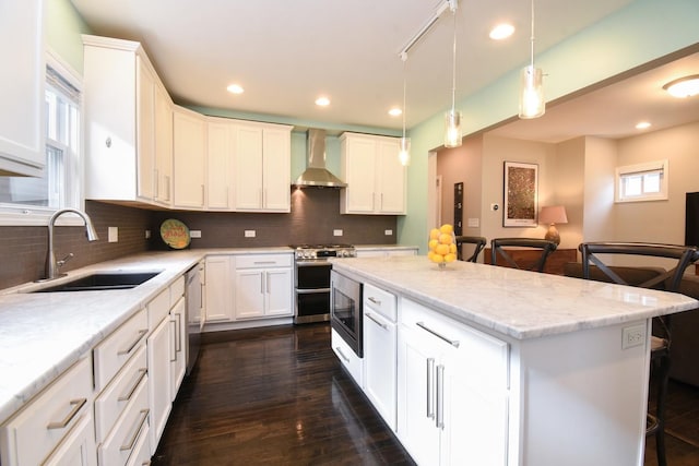 kitchen featuring white cabinetry, sink, a center island, stainless steel appliances, and wall chimney exhaust hood