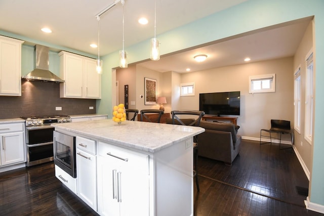 kitchen with white cabinetry, decorative light fixtures, a center island, appliances with stainless steel finishes, and wall chimney range hood