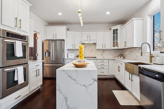 kitchen featuring light stone counters, stainless steel appliances, white cabinets, a sink, and under cabinet range hood