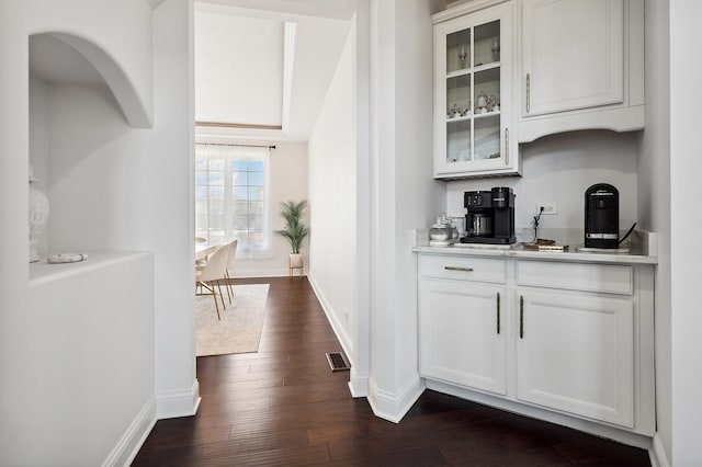 bar featuring dark wood-style floors, arched walkways, visible vents, and baseboards