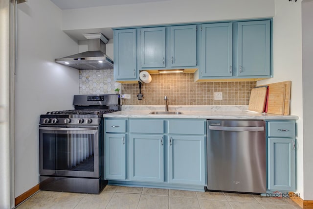 kitchen featuring blue cabinetry, wall chimney exhaust hood, sink, appliances with stainless steel finishes, and decorative backsplash