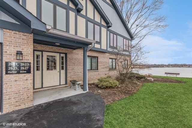 view of exterior entry with a water view, a lawn, and brick siding