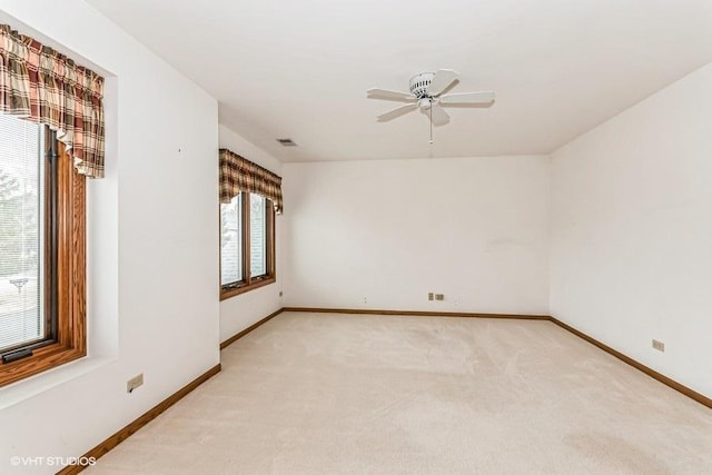 empty room featuring a ceiling fan, light colored carpet, visible vents, and baseboards