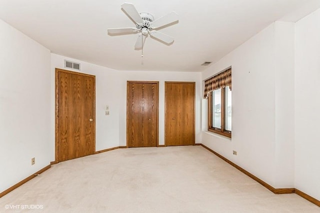 unfurnished bedroom featuring multiple closets, visible vents, light carpet, and baseboards