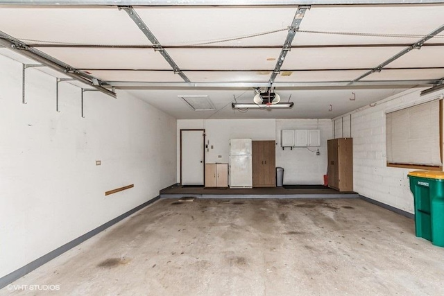 parking garage with a garage door opener, freestanding refrigerator, and baseboards