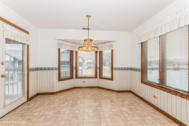 empty room with a wainscoted wall, an inviting chandelier, visible vents, and wallpapered walls