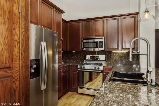 kitchen with sink, dark stone countertops, pendant lighting, stainless steel appliances, and backsplash