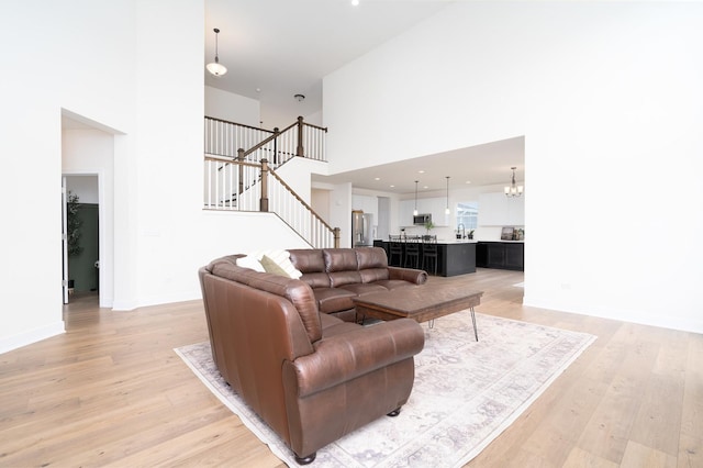 living room with a towering ceiling, a notable chandelier, and light wood-type flooring