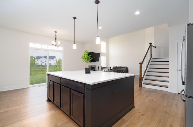 kitchen with pendant lighting, stainless steel refrigerator, a center island, light hardwood / wood-style floors, and dark brown cabinets