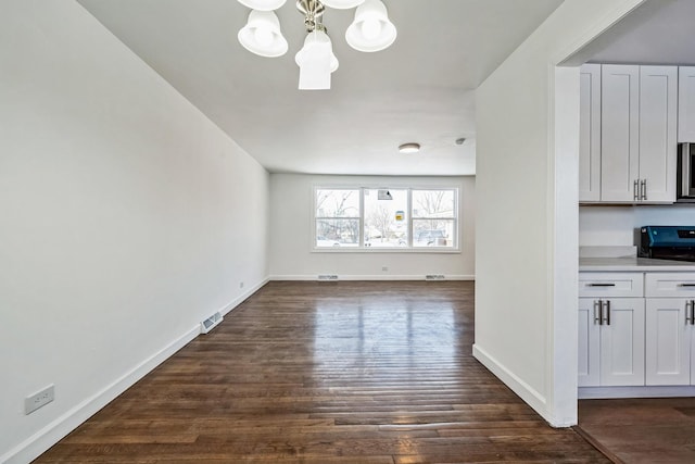 unfurnished living room with a notable chandelier and dark hardwood / wood-style flooring