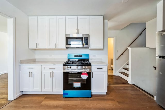 kitchen with hardwood / wood-style flooring, stainless steel appliances, light stone counters, and white cabinets