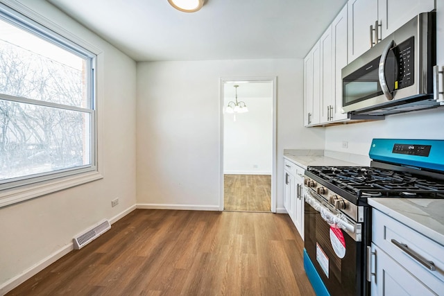 kitchen with stainless steel appliances, white cabinetry, hardwood / wood-style floors, and light stone counters