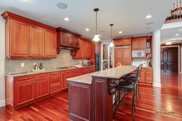 kitchen with dark wood-type flooring, a breakfast bar, decorative backsplash, arched walkways, and built in microwave