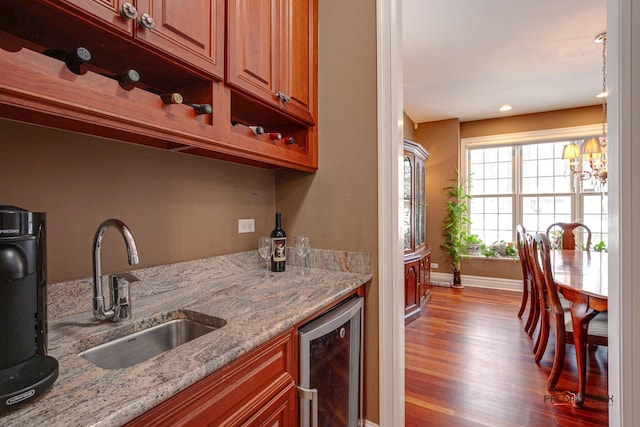 kitchen with wine cooler, light stone countertops, wood finished floors, and a sink