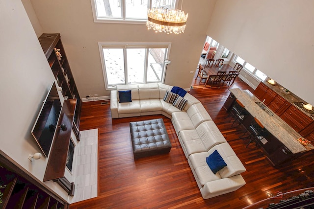 living room with a wealth of natural light, a high ceiling, an inviting chandelier, and wood finished floors