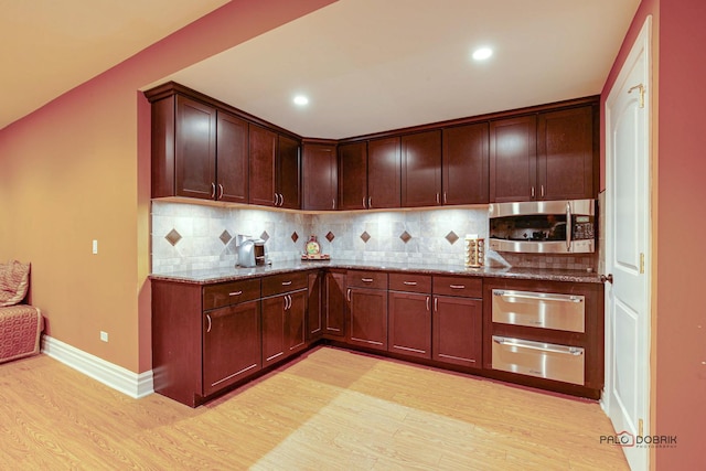 kitchen with a warming drawer, stainless steel microwave, light wood-type flooring, and light stone countertops