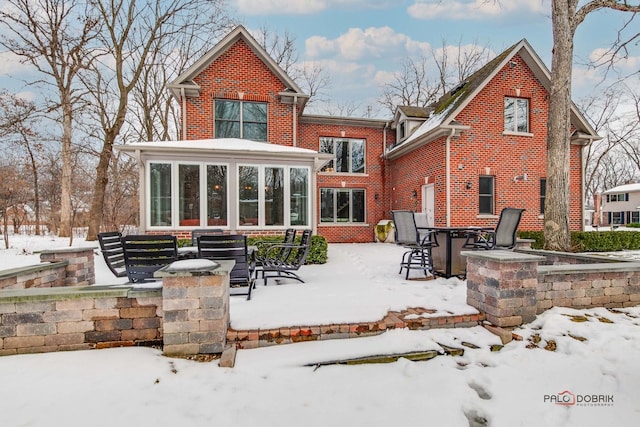 snow covered rear of property featuring a patio area, brick siding, and a sunroom