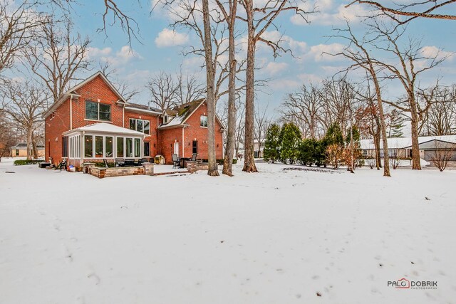 snow covered rear of property with brick siding and a sunroom