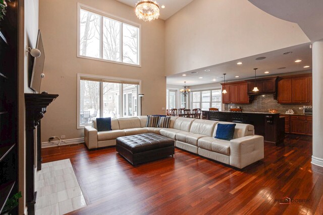 living area with a notable chandelier, recessed lighting, baseboards, a towering ceiling, and dark wood-style flooring