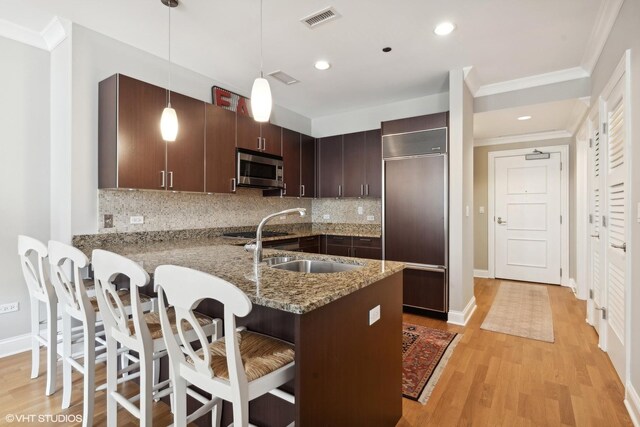 kitchen with a breakfast bar, paneled built in refrigerator, hanging light fixtures, dark brown cabinetry, and kitchen peninsula