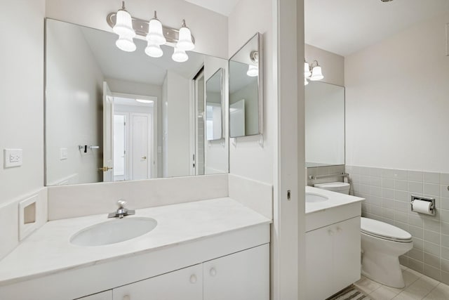 bathroom with tile patterned floors, toilet, tile walls, wainscoting, and vanity